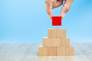 Close-up hand choose a red wooden block toy stacked in pyramid shape without graphics for Business...