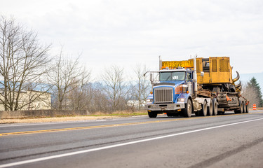 Blue big rig heavy duty semi truck with oversize load equipment on the step down semi truck moving...