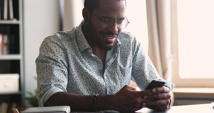 Smiling young african guy using mobile apps sit at table