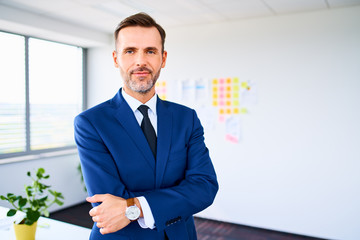Shot of positive mature businessman standing in modern office with crossed arms