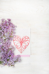Fototapeta premium Background with lilac flowers and decorative heart on white wooden table. Concept for Valentine's Day, Happy Mothers Day Greetings card. copy space