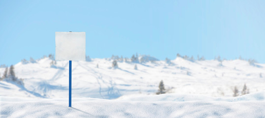 Blank sign for skiers on a ski slope pinned to the snow mockup. Copy space beside. Ski slopes and snowy peaks in background