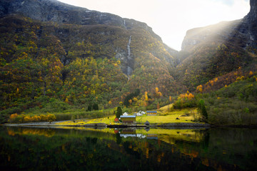 Fototapeta na wymiar Small village on the waterfront and mountains in the autumn season that reflect the water. Watch from a boat trip to see the beauty of Sognefjord Cruise, program from Gudvangen to Flam in Norway.