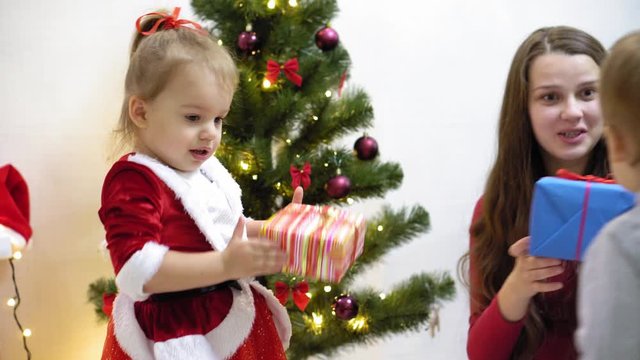 baby and pregnan mom hang red ball toy on Christmas tree. happy childhood concept. child and mother decorate tree with christmas balls. small child and a parent are playing by Christmas tree.