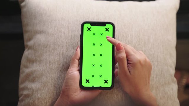 Close up of a woman's hand holding a mobile telephone with green screen in home. Top view chroma key smartphone technology, cell phone scrolling by hand concept. 