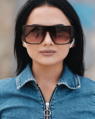 One Beautiful Brunette Girl Dressed in Denim Overalls Uses Mobile Bluetooth Earphones