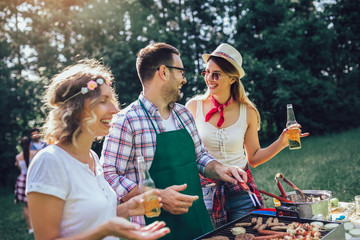 Group of friends stand at a barbecue, one cooking at grill