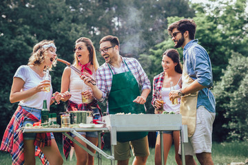 Group of friends stand at a barbecue, one cooking at grill