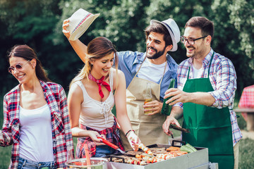 Group of friends stand at a barbecue, one cooking at grill