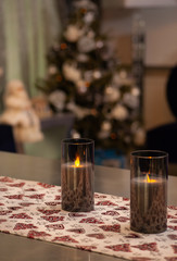 Obraz na płótnie Canvas A tablecloth with Christmas pattern on modern designer table with modern candles on it and decorated Christmas tree on the back