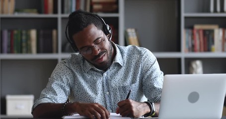 Smiling african male student wear headset elearning making notes - Powered by Adobe