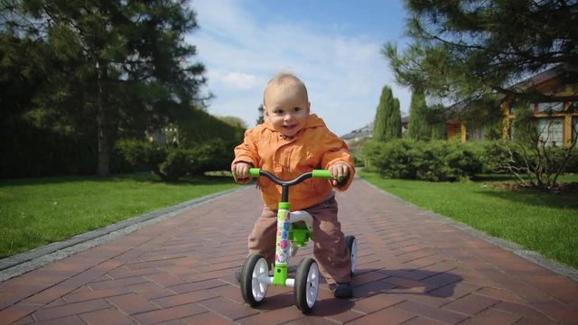 Happy toddler bicycling in slow motion. Smiling kid riding bike at park.