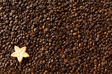 Background filled with a lot roasted coffee beans and a cookie
