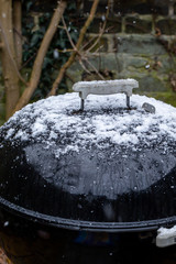 Kettle drum barbecue covered in snow while it is snowing in a UK garden