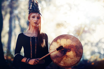 beautiful shamanic girl playing on shaman frame drum in the nature.