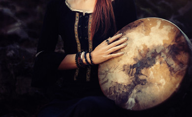 beautiful shamanic girl playing on shaman frame drum in the nature.