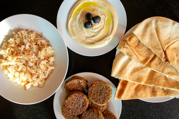 Famous traditional Arabic, Middle East, Israel cuisine. Tahini sauce, pita bread, rice and falafel on dark wooden background. Flat lay, top view. 