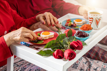 Hands of an elderly couple enjoying their breakfast at the bed. St Valentine’s concept.