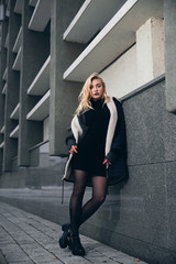 Girl in a black dress in the winter on a background of a dark building