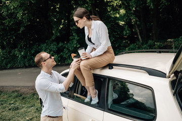 Young Happy Couple Dressed Alike in White T-shirt Having Fun Near the Car, Weekend Outside the City, Holidays and Road Trip Concept