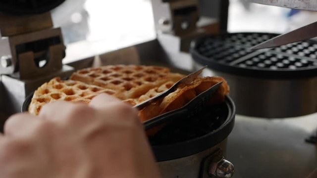 Chefs hands takes golden brown Belgian waffles from a waffle iron. Chef step by step preparing Belgian waffles with bananas, strawberries, ice cream, honey and chocolate syrup