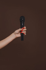 female hand with a microphone on a brown background, close-up, copy space