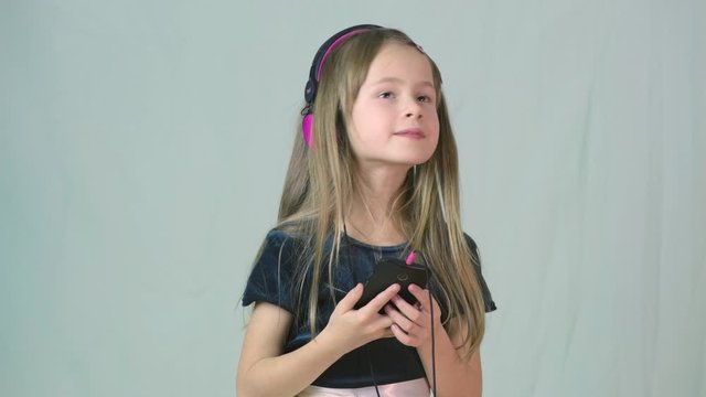 Pretty smiling cild girl listening to music in big pink earphones.
