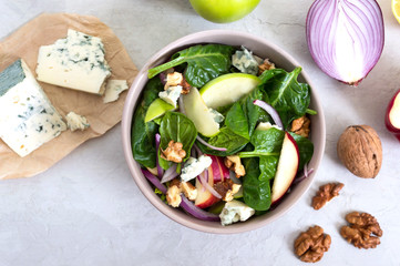 Delicious diet fitness salad with spinach, apples, red onions, blue cheese, nuts. Proper nutrition. Light concrete background. Top view.