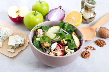 Delicious diet fitness salad with spinach, apples, red onions, blue cheese, nuts. Proper nutrition. Light concrete background.