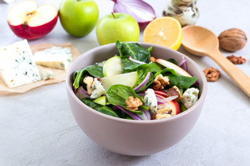 Delicious diet fitness salad with spinach, apples, red onions, blue cheese, nuts. Proper nutrition. Light concrete background.
