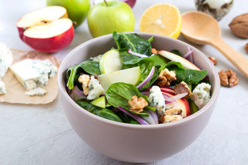 Delicious diet fitness salad with spinach, apples, red onions, blue cheese, nuts. Proper nutrition. Light concrete background.