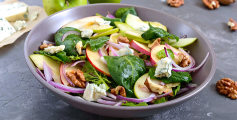 Tasty diet fitness salad with spinach, apples, red onions, blue cheese, nuts. Proper nutrition. Light concrete background