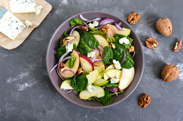 Tasty diet fitness salad with spinach, apples, red onions, blue cheese, nuts. Proper nutrition. Light concrete background. Top view.