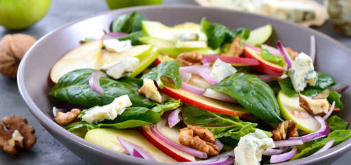 Tasty diet fitness salad with spinach, apples, red onions, blue cheese, nuts. Proper nutrition. Light concrete background