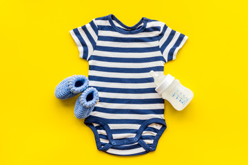 Blue bodysuit for baby boy near children's accessories on yellow background top-down
