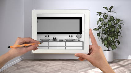 Hands holding and drawing on tablet showing modern bathroom with double sink and mirror CAD sketch. Real finished interior in the background, architecture design presentation