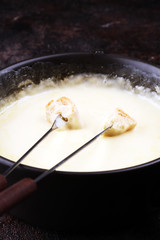 Gourmet Swiss fondue dinner on a winter evening with assorted cheeses on a board alongside a heated pot of cheese fondue with two forks dipping