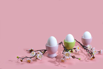 Easter eggs with branches of blooming cherry on a pink background, minimalistic concept.