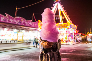 Hidden woman with pink strawberry cotton candy at night luna park - people have fun in nightlife at the event in the city