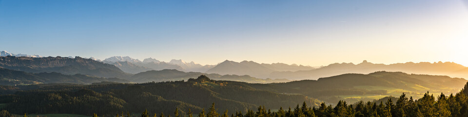 swiss mountain range in switzerland while the valley is covered in fog during sunset, super warm light and clear sky