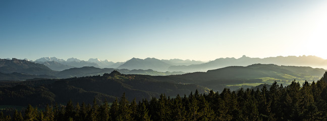 swiss mountain range in switzerland while the valley is covered in fog during sunset, super warm light and clear sky