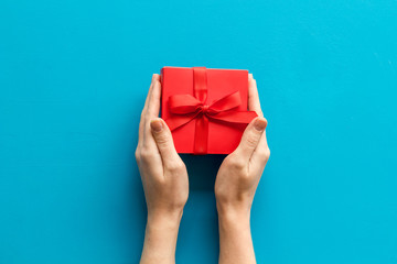 Give a gift on Valentine's Day. Women hand hold beautiful red present box on blue background top-down copy space