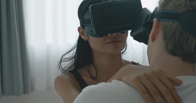 Close up of lover using virtual reality trying to have sex in bed, close up of face smile. Caucasian male with his girlfriend in black mask, asian woman in black lingerie. Future cyber sex concept.
