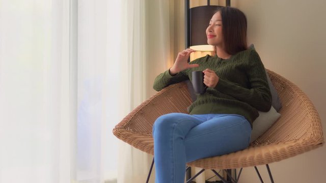 Beautiful smiling Asian woman enjoy cup of coffee on modern armchair