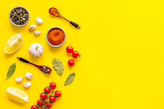 Kitchen frame with spices and food - pepper, garlic, cherry tomatoes - on yellow background top-down frame copy space