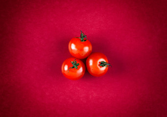 Three cherry tomatoes on red background.