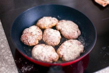 Homemade cutlets in frying pan cooking on the induction hob.