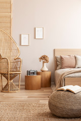 Open book on beige pouf in simple bedroom interior with peacock chair and single bed