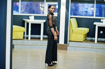 Charming african american woman in black formal wear posing at restaurant.