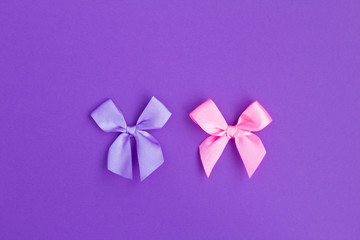 Pink and violet bows in the center of  the violet background. Top view. Copy space. Holiday background.